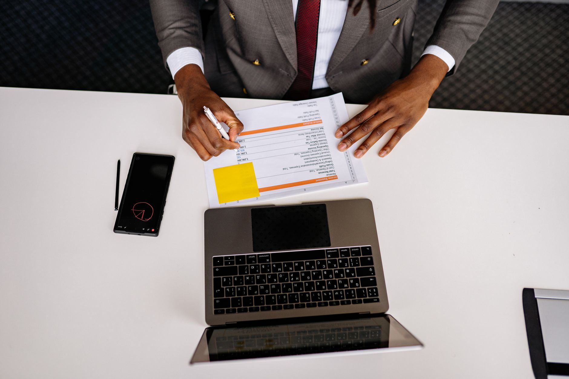 Top view of a business professional analyzing documents with a laptop on a white desk in an office setting.